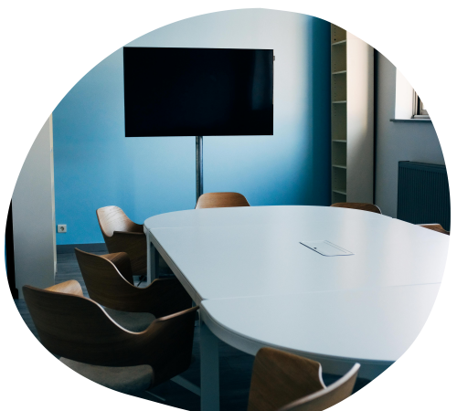 A bright and spacious conference room with a rectangular table, comfortable chairs, and a flat-screen TV mounted on the wall.